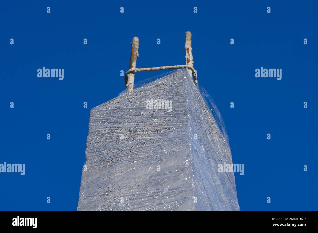 Colonna in calcestruzzo non finita sotto la torre con barra di rinforzo in acciaio sporgente e con involucro in plastica trasparente per mantenere la temperatura Foto Stock