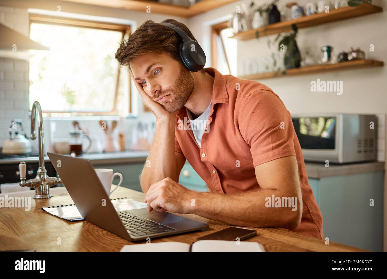 Giovane uomo d'affari caucasico serio che indossa cuffie e ascolta musica mentre lavora su un computer portatile da sola. Un uomo d'affari stressato Foto Stock
