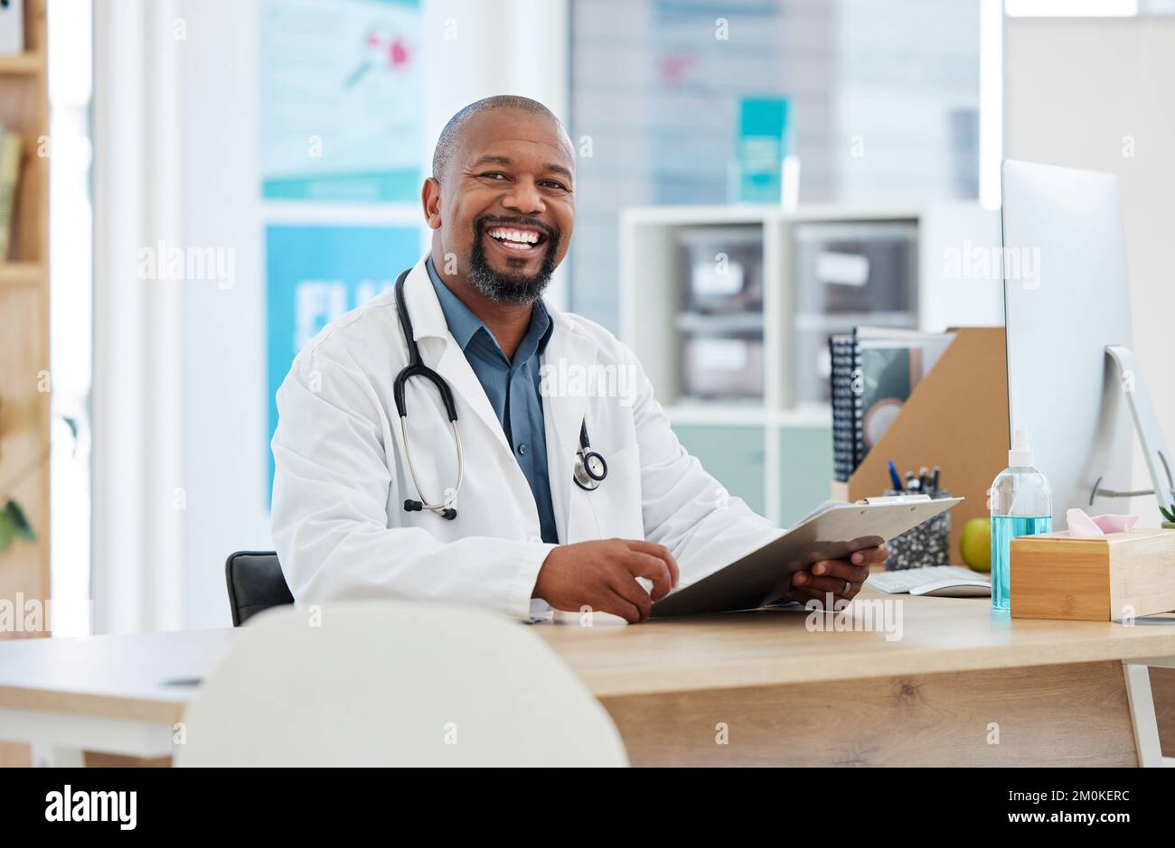Bel medico nel suo ufficio. Medico afro-americano che legge una tabella dei pazienti. Professionista medico maturo che legge le informazioni del paziente. Medico Foto Stock