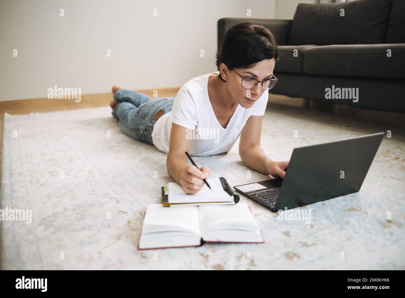 Donna lavora su un notebook da casa. Attraente brunetta di mezza età con computer sul tappeto Foto Stock