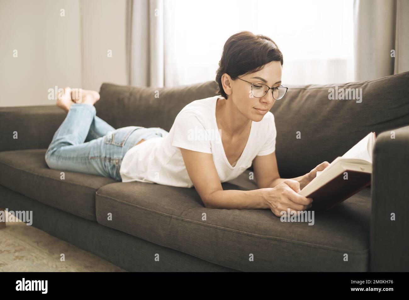 Donna allegra che legge un libro a casa. Brunetta con capelli corti in abiti casual Foto Stock