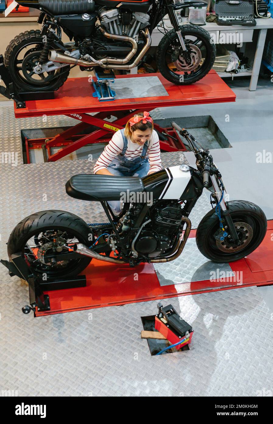 Donna meccanica che rivede motocicletta personalizzata in fabbrica Foto Stock