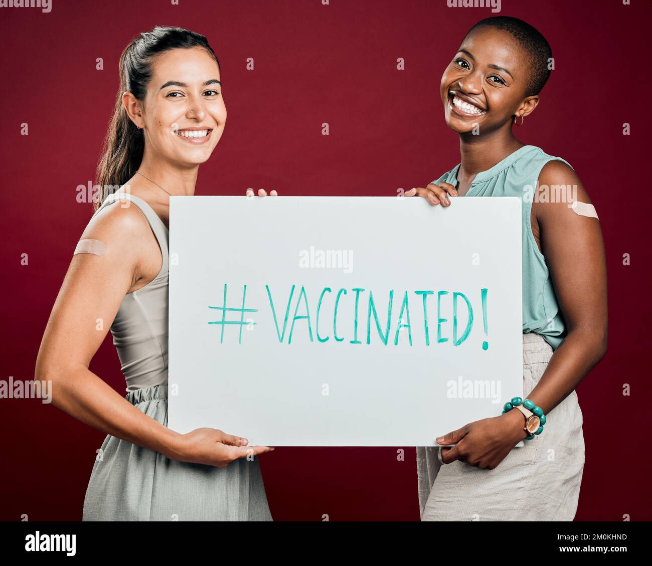 Covid ha vaccinato le donne di razza afro-americana e mista mostrando e tenendo il manifesto. Due persone isolate su sfondo rosso studio con copyspace Foto Stock