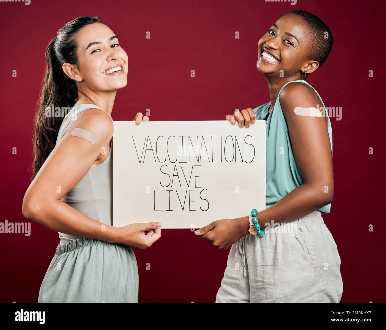 Covid ha vaccinato le donne di razza afro-americana e mista mostrando e tenendo il manifesto. Due persone isolate su sfondo rosso studio con copyspace Foto Stock