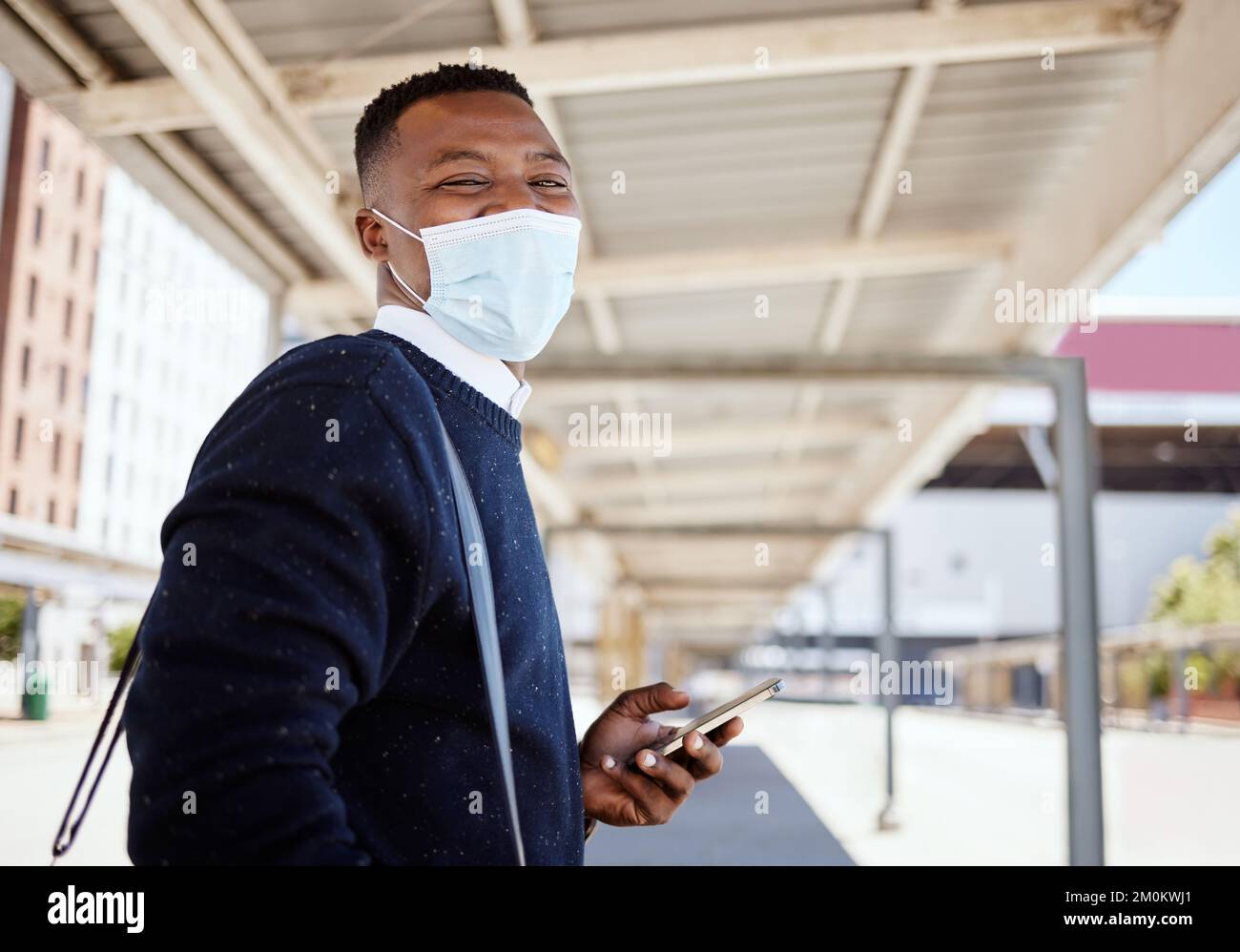 Uomo d'affari nero che viaggia da solo. Un giovane uomo d'affari afroamericano in attesa di un treno in una stazione ferroviaria e utilizzando il suo cellulare wireless Foto Stock