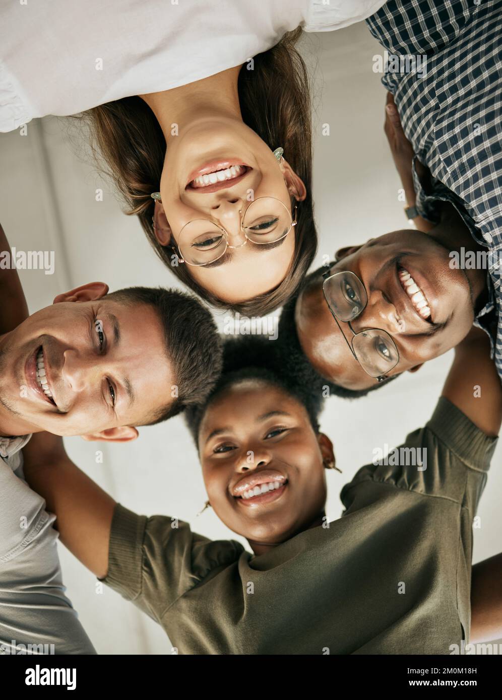 Il team di creativi si è riunito in un'unità. Felice team di business diversificato in piedi in cerchio abbracciando l'un l'altro e sorridendo, dal basso Foto Stock