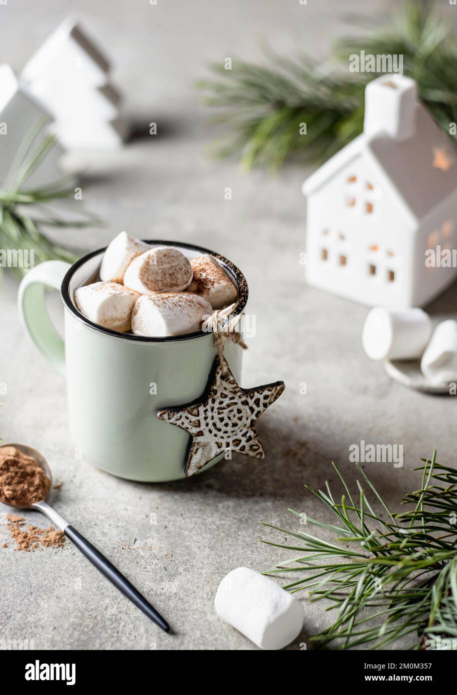 Bevanda calda cacao o caffè con marshmallows in tazza. Rami di abete, casa in ceramica sullo sfondo. Concetto di tempo di inverno. Vacanze stagionali accoglienti. Verticale Foto Stock