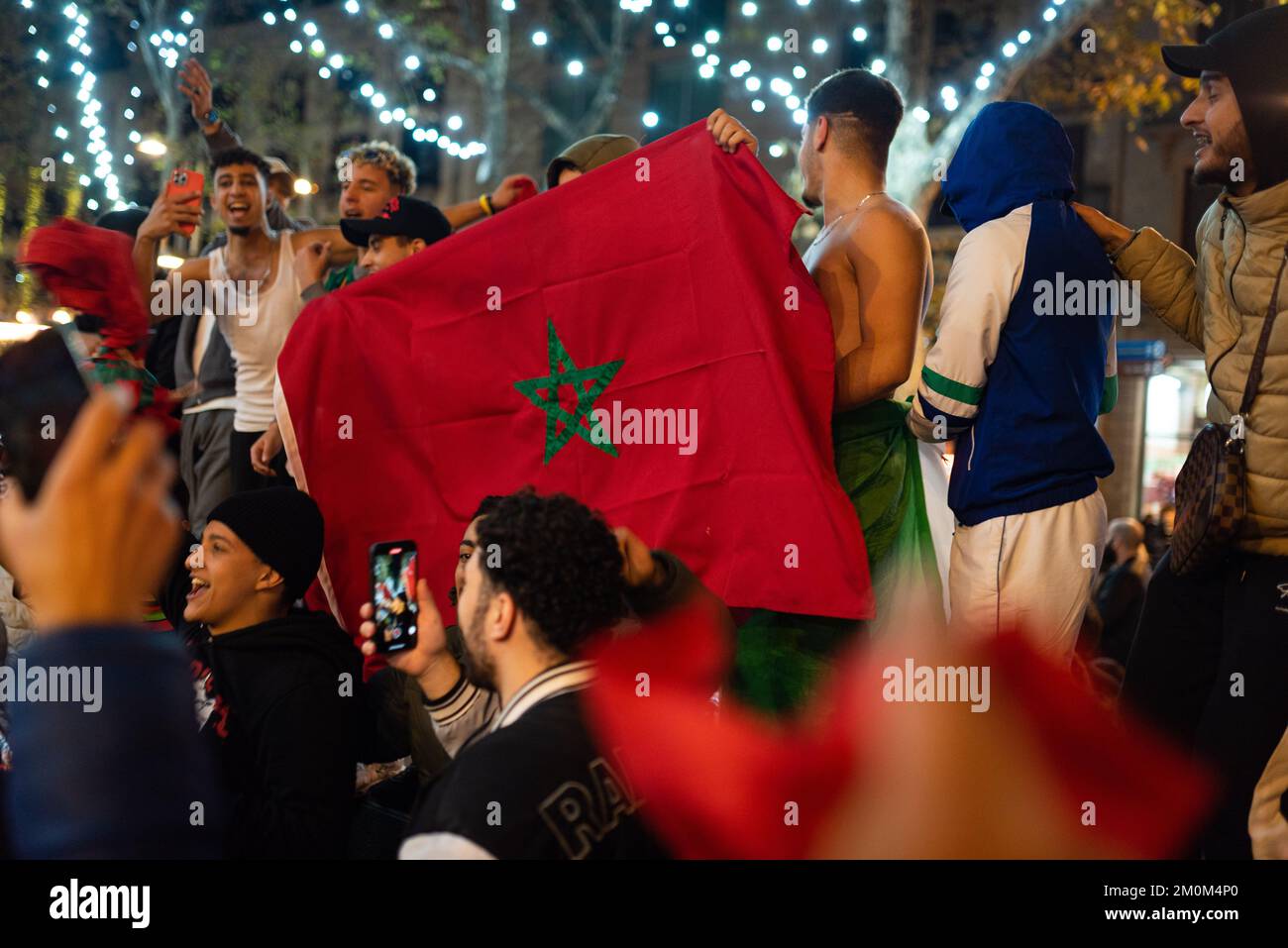 Barcellona, Spagna. 06th Dec, 2022. Un gruppo di giovani marocchini tiene una bandiera marocchina mentre festeggiano la vittoria della squadra di calcio del Marocco sulla Spagna nel centro della città dopo la partita di calcio. In una vittoria a sorpresa, la squadra marocchina ha battuto la Spagna alle penalità, passando ai quarti di finale, dove affronterà il Portogallo, per la prima volta nella sua storia. Credit: SOPA Images Limited/Alamy Live News Foto Stock
