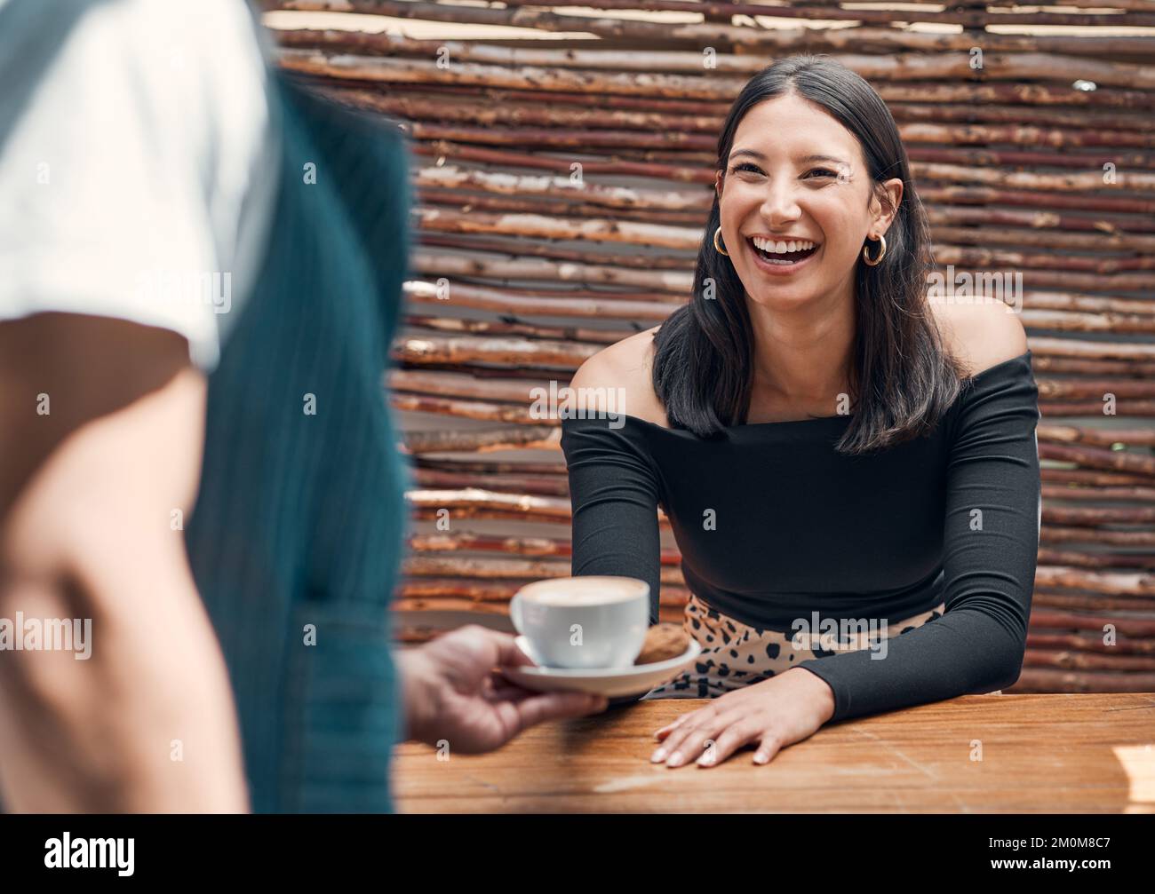 Felice giovane donna ispanica che riceve una tazza di caffè da un cameriere in un bar locale. Donna di razza mista entusiasta di essere servita il suo latte caldo o cappuccino Foto Stock