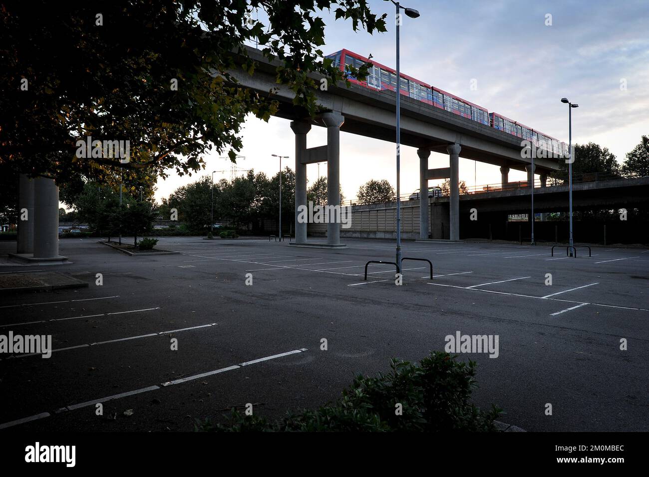 Un treno sulla Docklands Light Railway automatica passa sopra un parcheggio vuoto a Dawn, nella zona est di Londra. Foto Stock