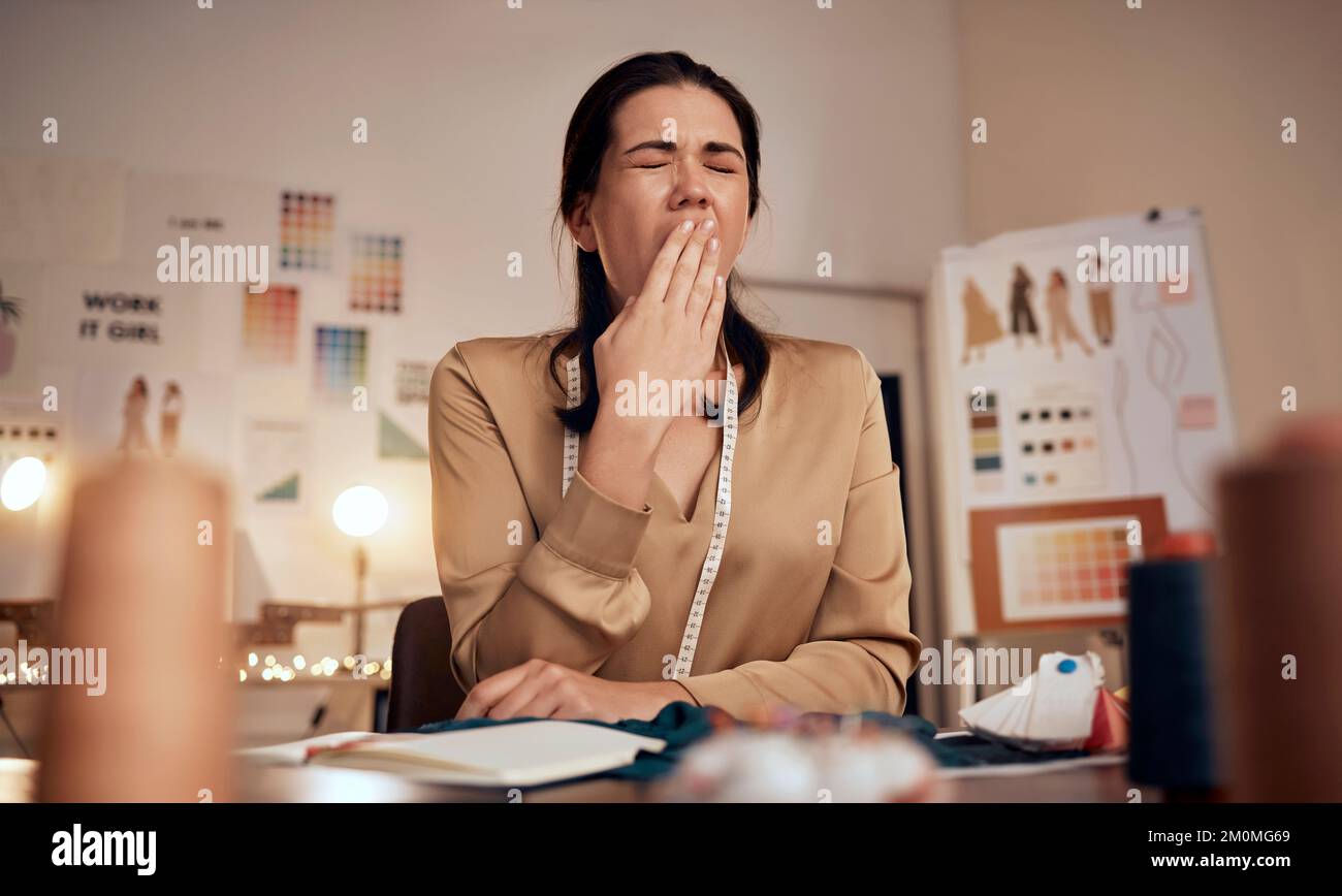 Stilista di moda stanco, donna e sbadiglio mentre lavora di notte in ufficio creativo, studio tessile o startup. Sarto esausto, assonnato e sovraccarico di lavoro Foto Stock