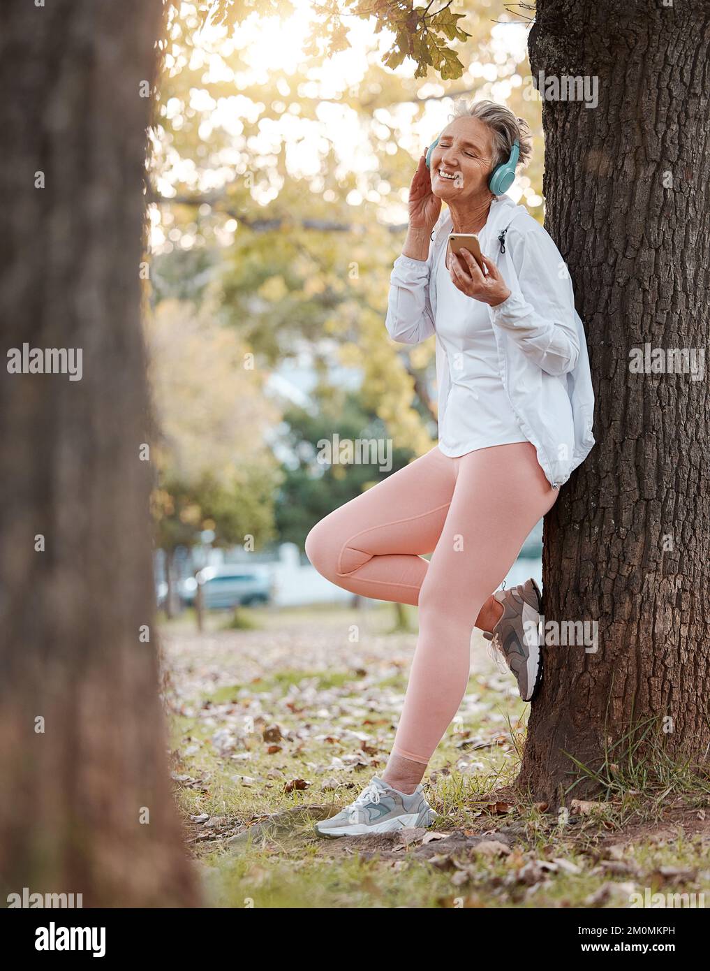 Smartphone, cuffie e donna anziana nel parco per musica benessere, salute mentale e pace nella natura con blog online, Internet o social media. Anziani Foto Stock