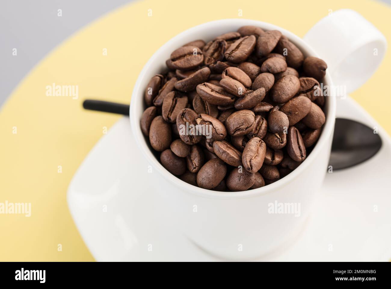 Tazza bianca piena di chicchi di caffè interi arrostiti e saporiti Foto Stock