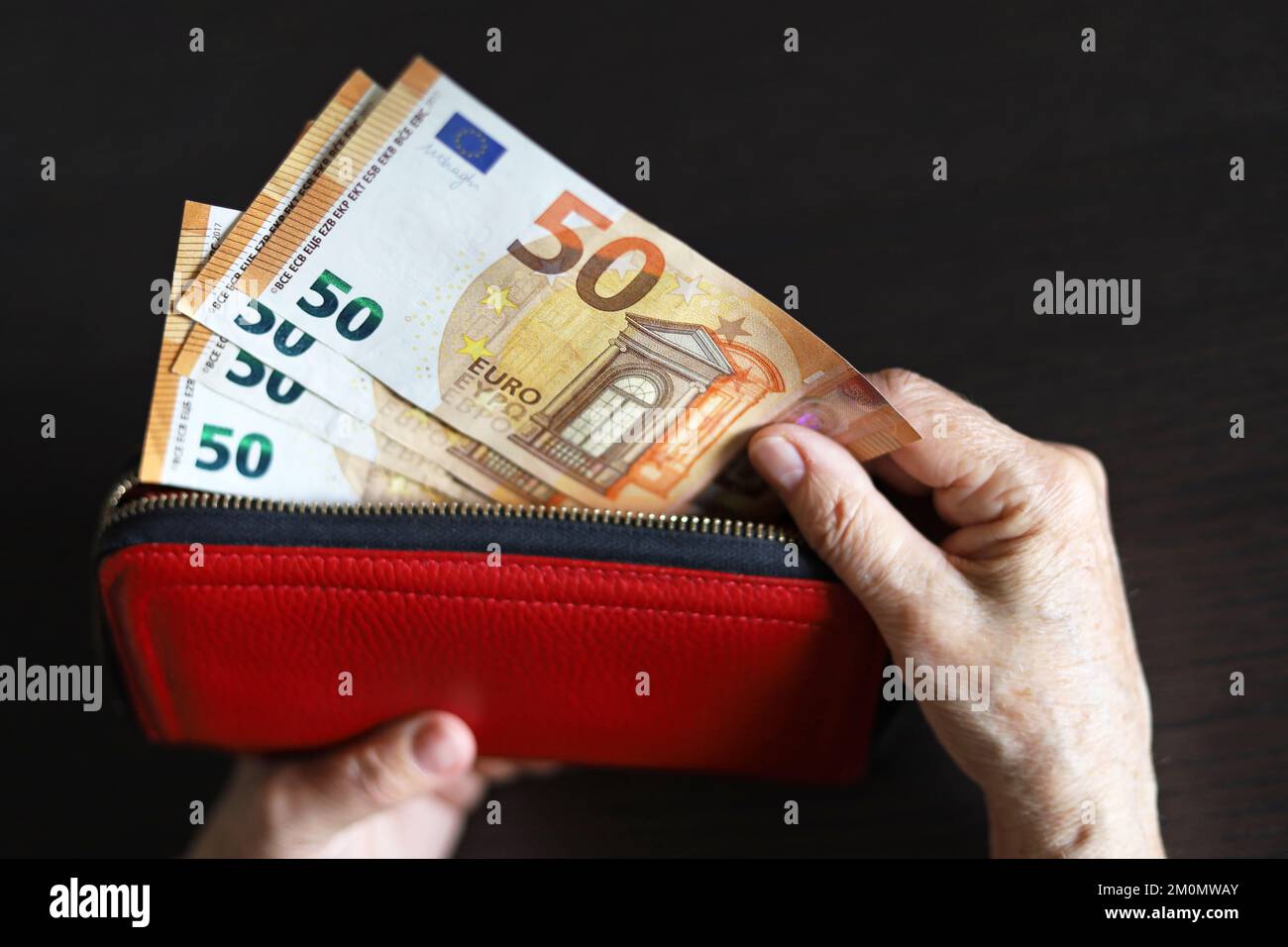 Banconote in euro in portafoglio rosso in mani stropicciate di donna anziana. Concetto di pagamenti e assistenza pensionistica, risparmio, pensionamento in Europa Foto Stock