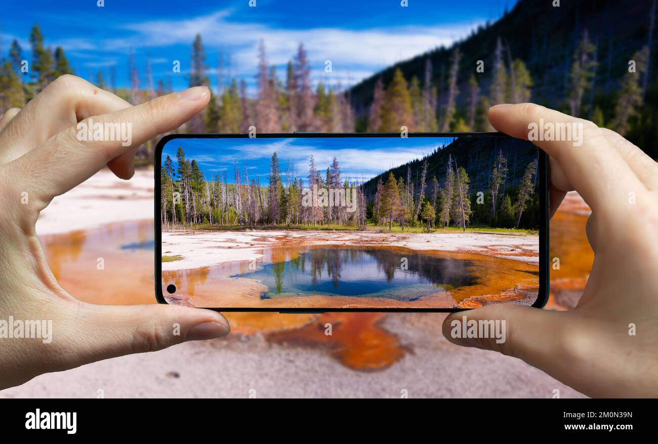 Turista scattare una foto con un telefono cellulare di una sorgente calda nel parco nazionale di Yellowstone, Stati Uniti. Foto Stock
