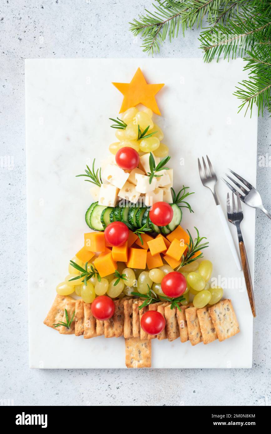 Piatto di formaggi a forma di albero di Natale con cracker, uva, formaggio, pomodori e salsa di mirtilli rossi, snack per le vacanze invernali. Vista dall'alto Foto Stock
