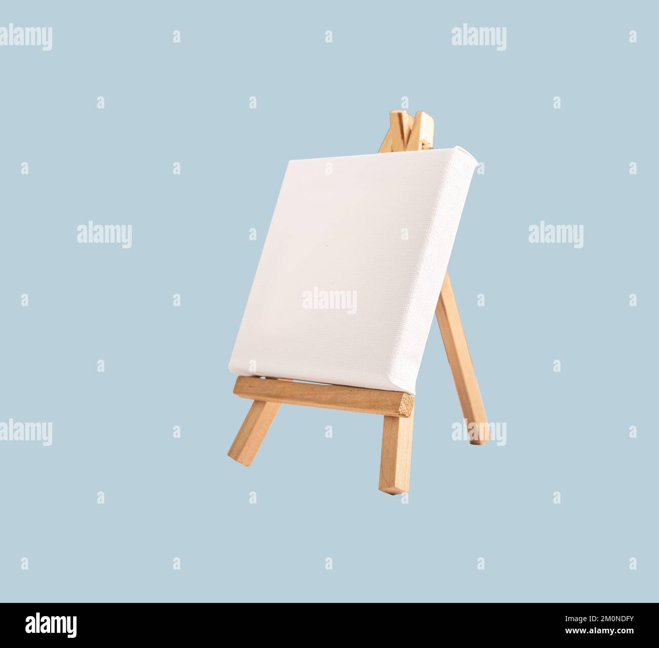 Bianco quadro tela mock up, carta bianca su mini treppiede di legno, cavalletto giocattolo su sfondo blu. Foto di alta qualità Foto Stock