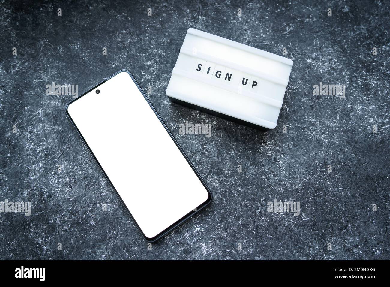Smartphone nero con schermo mockup bianco e testo di registrazione su scatola luminosa con lettere su sfondo di cemento scuro. Foto Stock