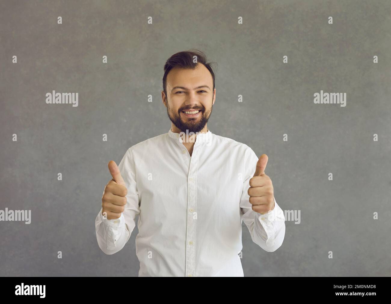 Ritratto di felice giovane uomo che dà pollici in piedi isolato su sfondo grigio Foto Stock