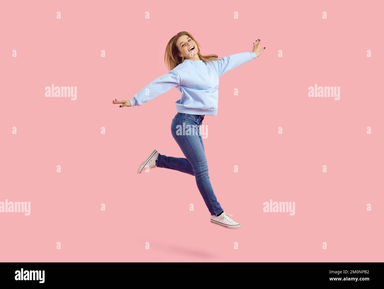 Giovane donna sorridente che si diverte a rimbalzare con le braccia tese su sfondo rosa pastello in studio. Foto Stock