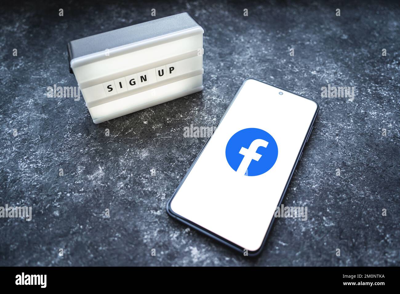 Logo dell'app Facebook sullo schermo nero dello smartphone e testo di registrazione su scatola luminosa su sfondo di cemento scuro. Cracovia, Polonia - 11 novembre 2022. Foto Stock