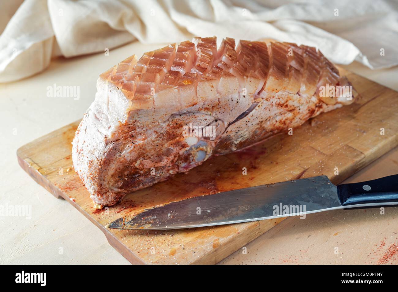 Pezzo di carne di maiale cruda con crosta grassa spazzolato con senape e spezie su un tavolo da cucina in legno, pronto per il forno per una deliziosa crosta arrosto Foto Stock