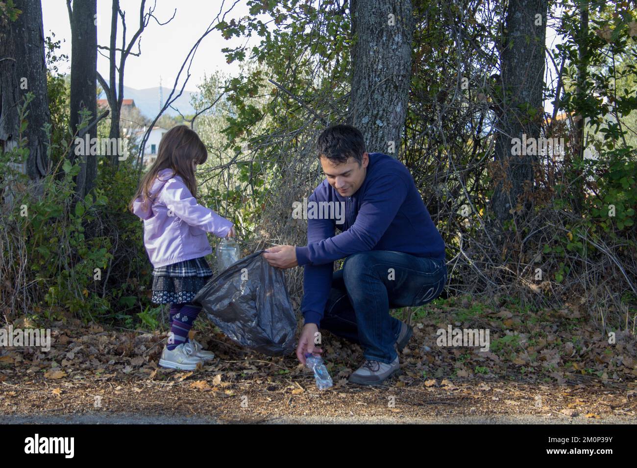 Padre e figlia nel bosco che raccoglie bottiglie di plastica. Pulizia e riciclaggio della natura. Salvaguardare il pianeta. Foto Stock