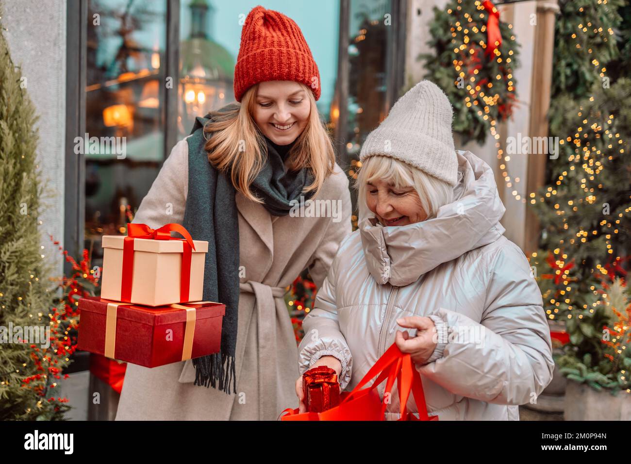 Due donne allegre stanno divertendosi nella strada della città a Natale, ridendo e comprando regali per i loro cari. Consumismo, shopping Foto Stock