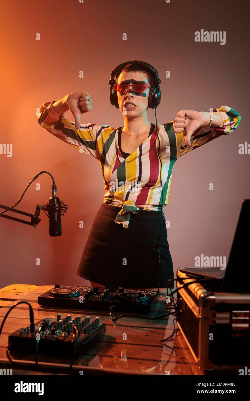 Disco jockey mostrando pollici giù segno in studio, facendo dispiacere e disapprovazione gesto dopo l'uso di giradischi e mixer per remix techno musica. Esprimere il rifiuto e il disaccordo alla parte. Foto Stock