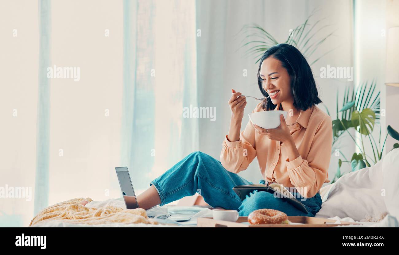 Colazione, computer portatile e donna che trasmettono un film per pranzo o brunch in una rilassante camera da letto della suite dell'hotel in vacanza. Sorridere e felice persona ama ridere Foto Stock