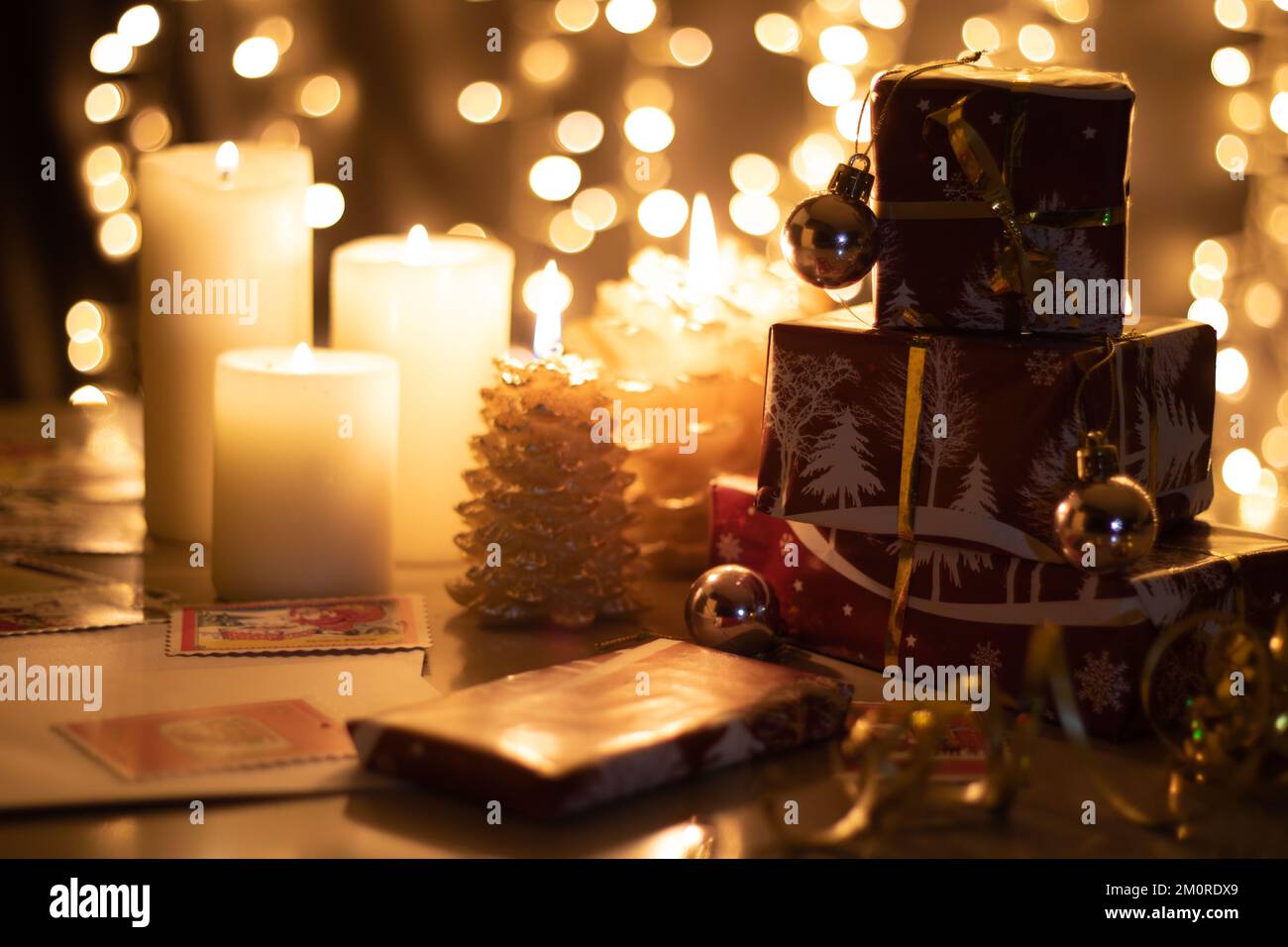 i regali avvolti da foto si trovano su un tavolo accanto alle candele con un bokeh di ghirlanda luminosa sullo sfondo Foto Stock