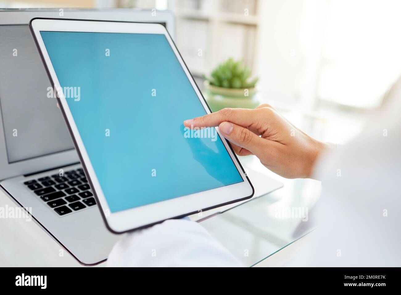 Donna di razza mista sconosciuta che usa un tablet e digita un'e-mail mentre si siede alla sua scrivania in un ospedale. Medico femminile che utilizza un dispositivo wireless durante l'uso Foto Stock