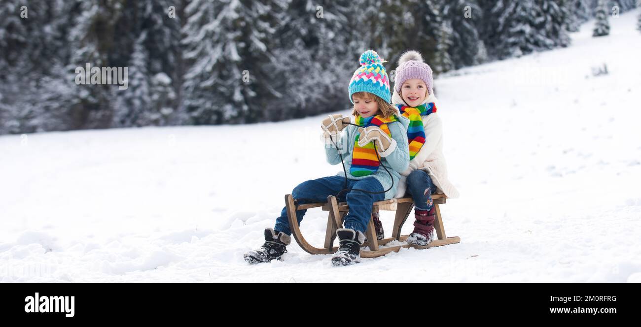 Amici bambini ragazzo e ragazza slittano in inverno. Bambini che si divertono con gli scivoli di neve in inverno. Figlio e figlia amano fare un giro in slitta. Foto Stock