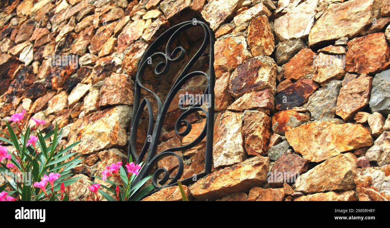 Robusto muro di pietra giallo e beige, adatto per sfondi e albero e fiore di oleandro Foto Stock