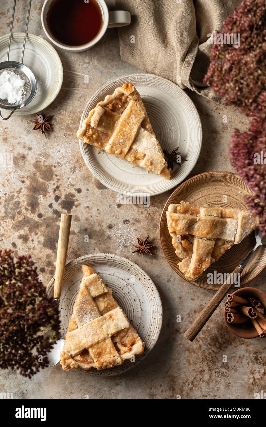 Tre porzioni di torta di mele americana con posate e tè, vista dall'alto tavolo scena su sfondo marrone textured. Giacitura piatta Foto Stock