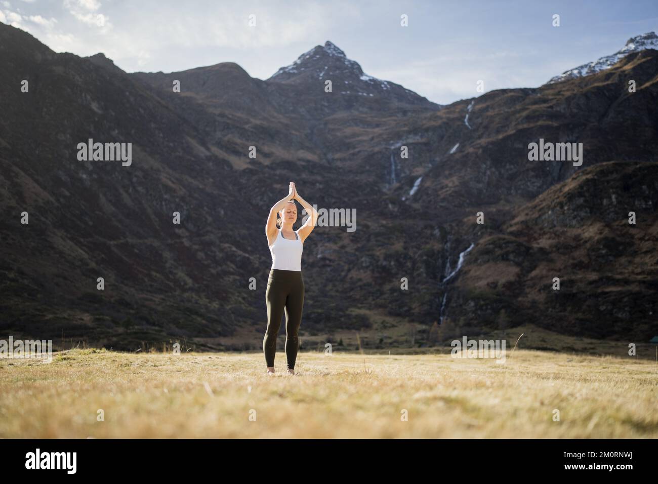 Donna in piedi in un prato alpino facendo yoga con le mani in posa di preghiera Gastein, Austria Foto Stock