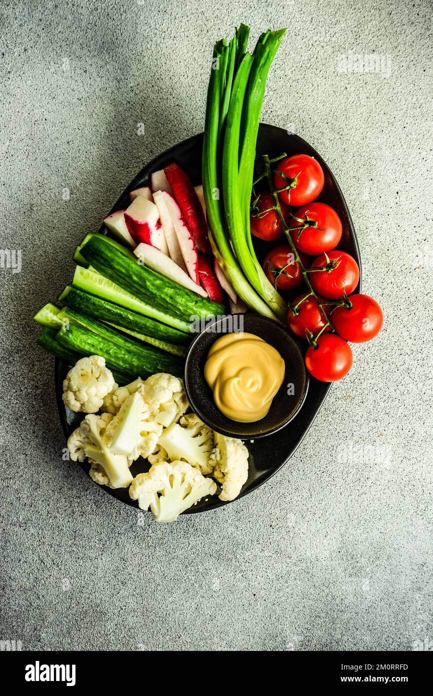 Vista dall'alto di una ciotola di cavolfiore crudo, cetriolo, ravanello, cipollina e pomodori ciliegini con salsa maionese Foto Stock