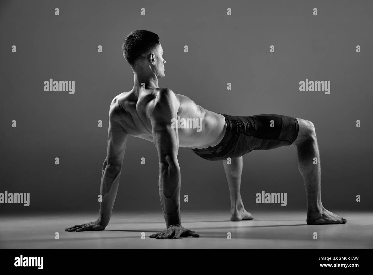 Riprese in bianco e nero di atleta muscolare flessibile maschile che mostrano elementi sportivi del flusso animale isolati su sfondo grigio. Fitness, sport alla moda Foto Stock