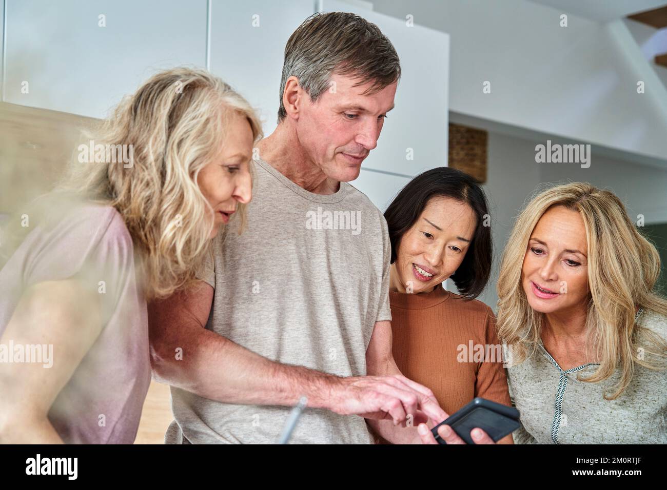 Gruppo eterogeneo di amici anziani che utilizzano lo smartphone in cucina Foto Stock