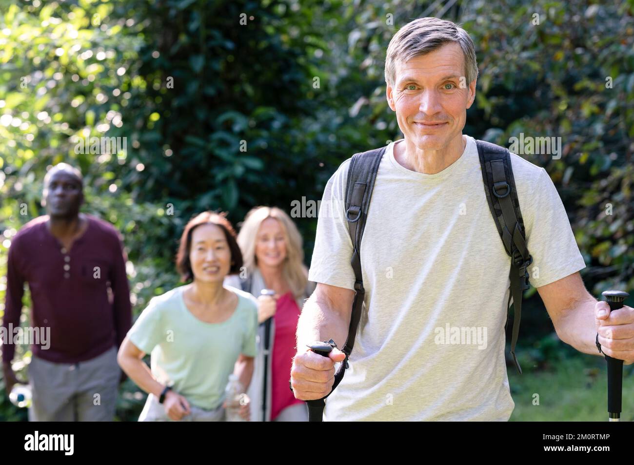 Bell'uomo di mezza età con bastoni da trekking e zaini per fare escursioni nelle strade secondarie locali con il suo variegato gruppo di amici Foto Stock
