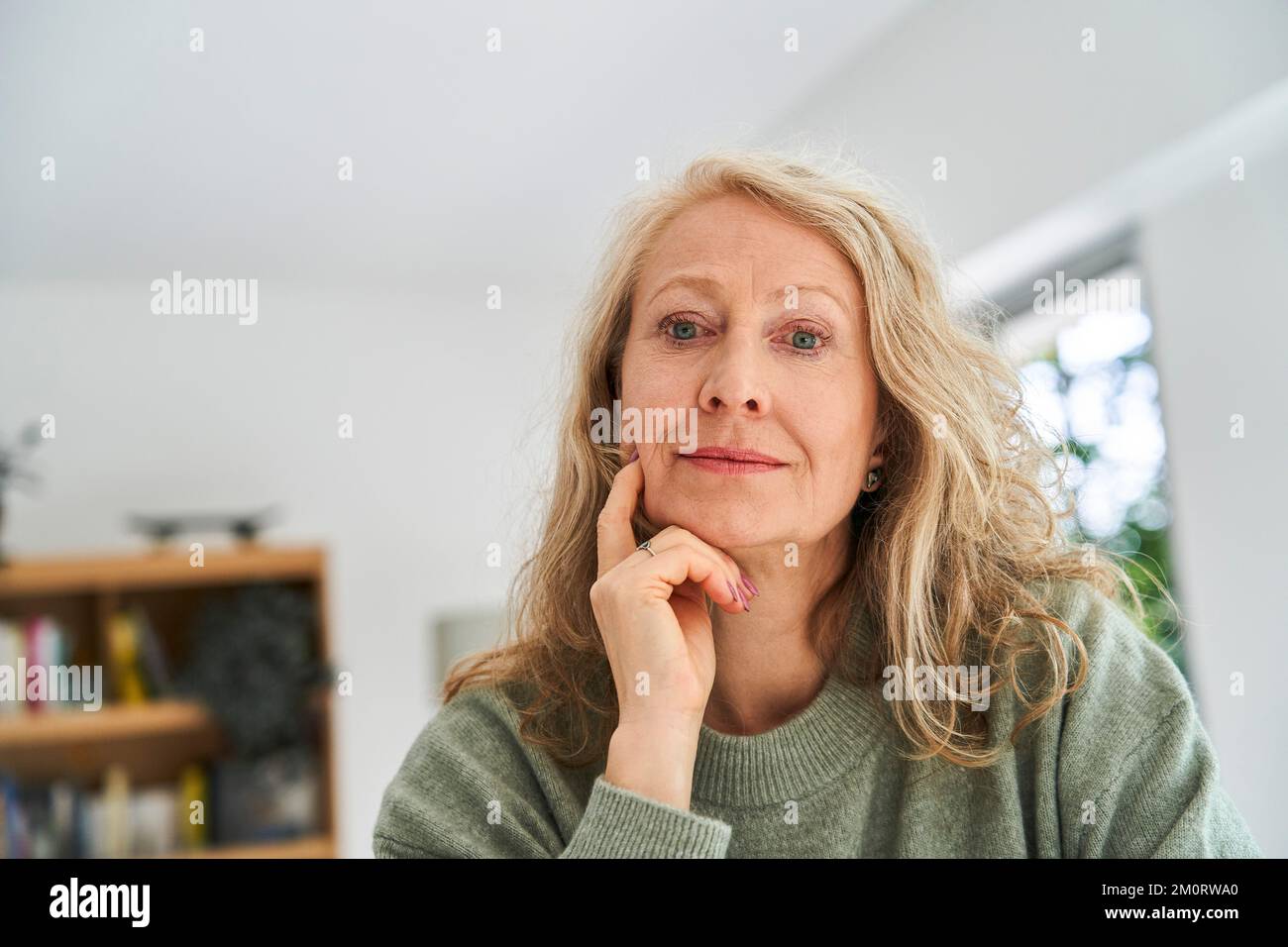 Donna anziana premurosa con la mano sul mento seduta nella sala da pranzo Foto Stock