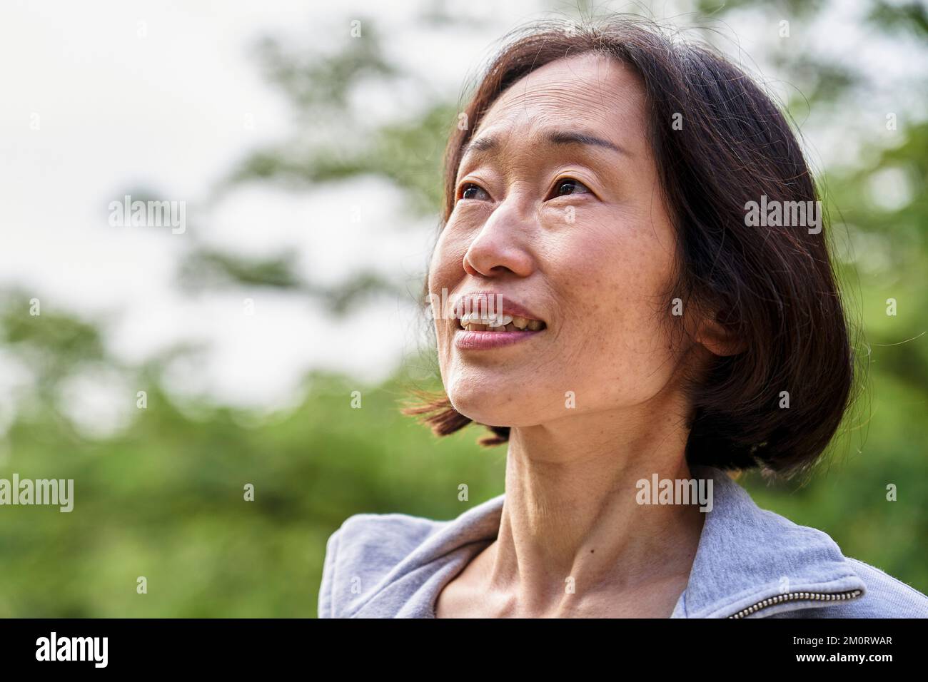 Donna asiatica anziana che guarda in alto mentre si trova all'aperto Foto Stock