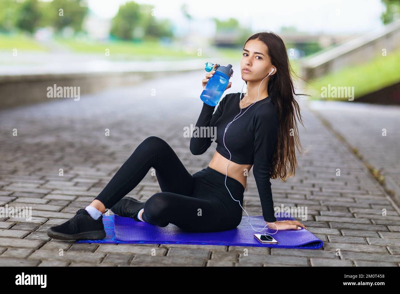 Giovane bella donna che conduce uno stile di vita sano ascoltare la musica mentre si siede su un tappeto e riposarsi dopo fare sport all'aperto Foto Stock