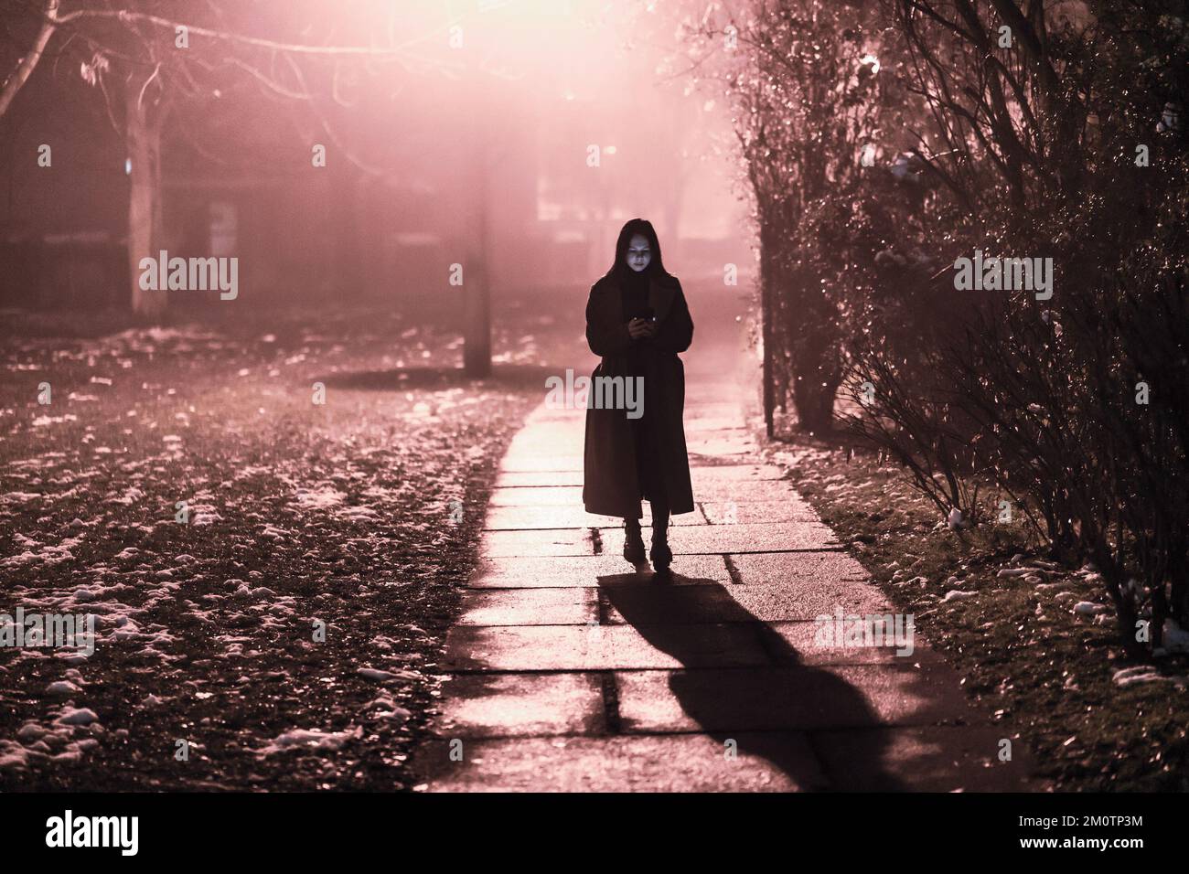 una giovane donna cammina per la città di notte e legge i messaggi su un telefono cellulare Foto Stock