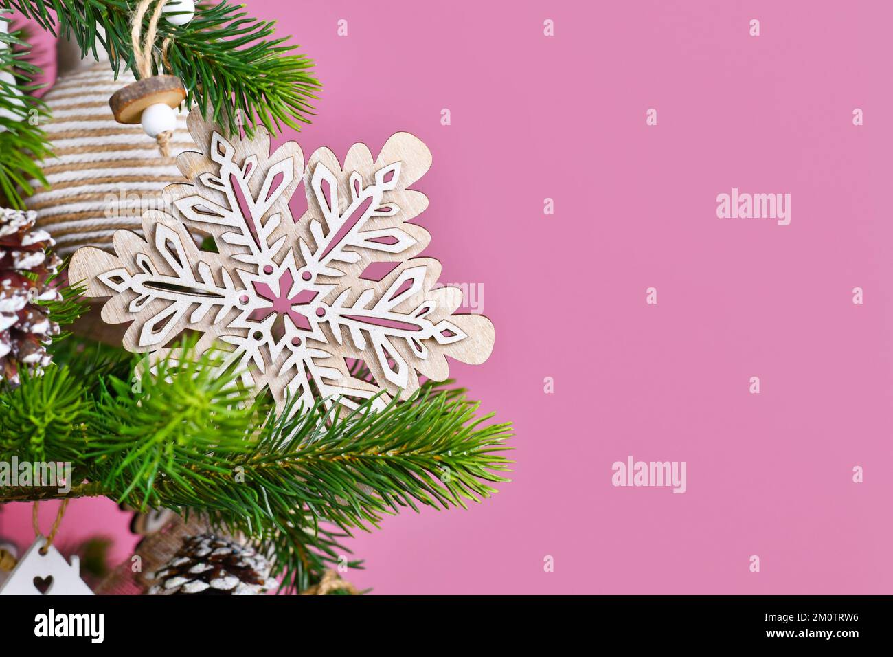 Ramo d'albero di Natale con ornamento in legno naturale fiocco di neve di fronte a sfondo rosa con spazio copia Foto Stock