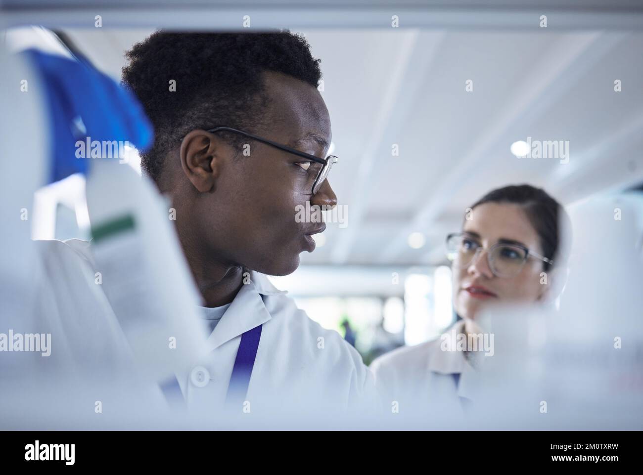 Giovane scienziato afroamericano che controlla i campioni con una collega femminile.due professionisti medici che lavorano insieme sugli esperimenti nel laboratorio Foto Stock