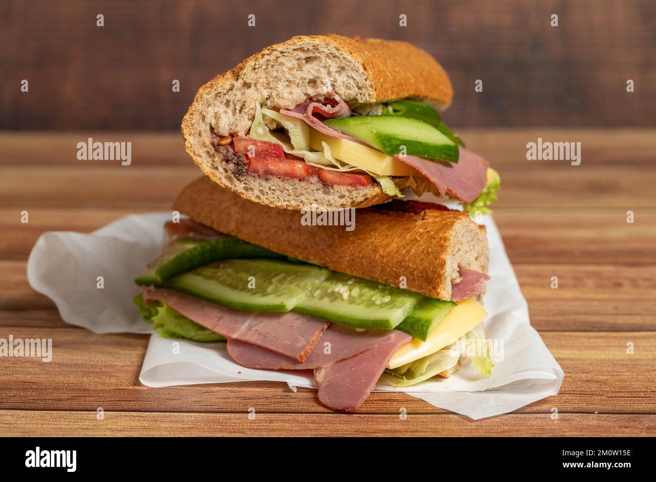 Sandwich baguette. Sandwich con salame, carne affumicata, olive, lattuga, pomodoro e cetriolo su fondo ligneo Foto Stock