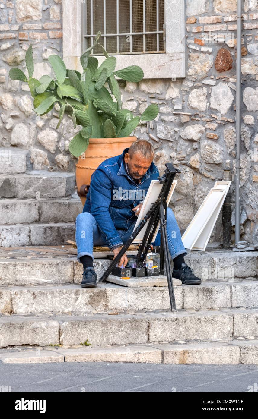 Artista con il cavalletto e le pitture, seduto su gradini a Taormina. Sicilia, Italia Foto Stock