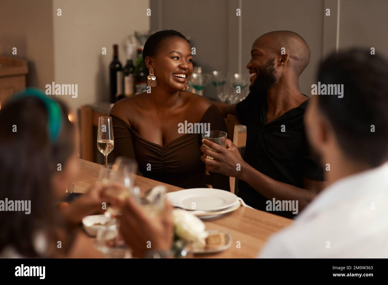 Coppia nera, champagne e festa con gli amici per Capodanno, cena di Natale o festa sociale in casa. L'uomo e la donna che parlano e. Foto Stock