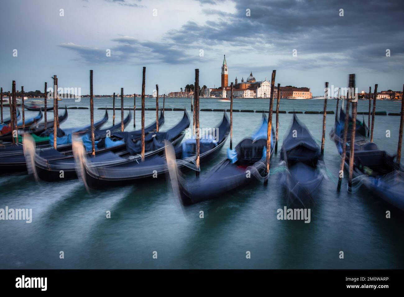 La gondola si trova parcheggiata lungo il lungomare di Piazza San Marco con l'isola di San Giorgio maggiore sullo sfondo della storica Venezia. Foto Stock
